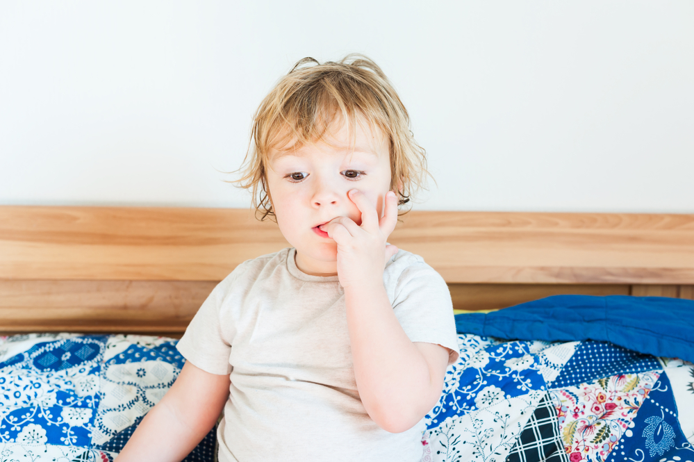 Interior portrait of a cute toddler boy biting nails