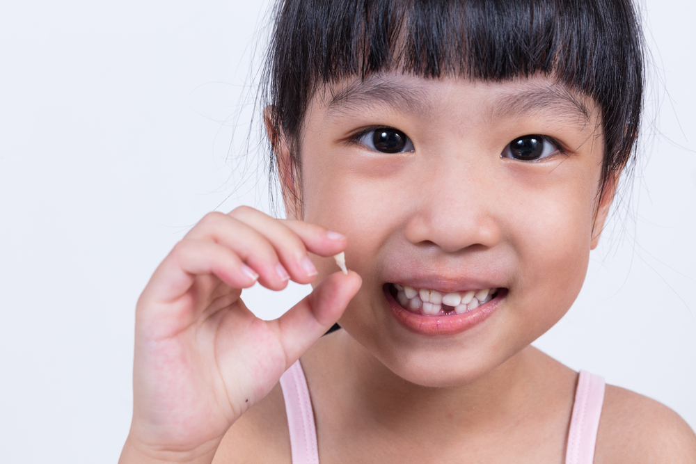 Asian Chinese little girl holding her missing tooth in isolated white background