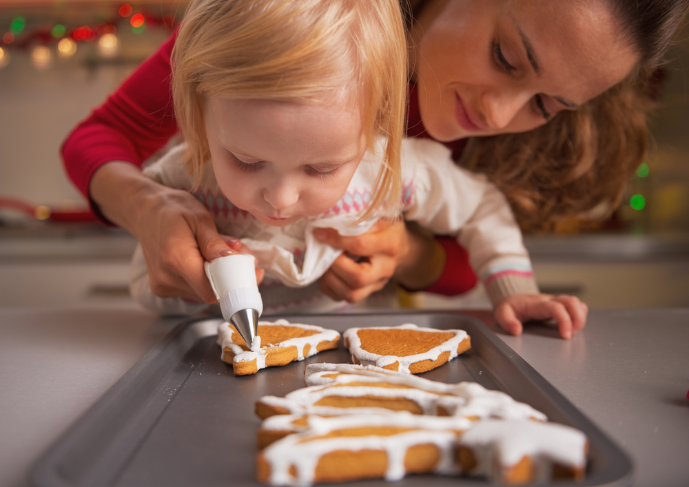 Baby helping mother decorate homemade christmas cookies with glaze Baby helping mother decorate homemade christmas cookies with glaze
